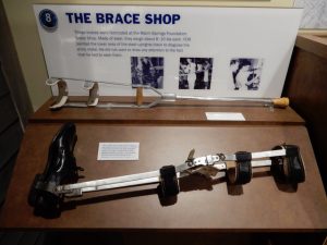 FDR's brace and crutch in a display case in a museum, sign talks about the brace shop.