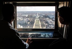 Two people looking out of the Washington Monument window at the capital and DC.